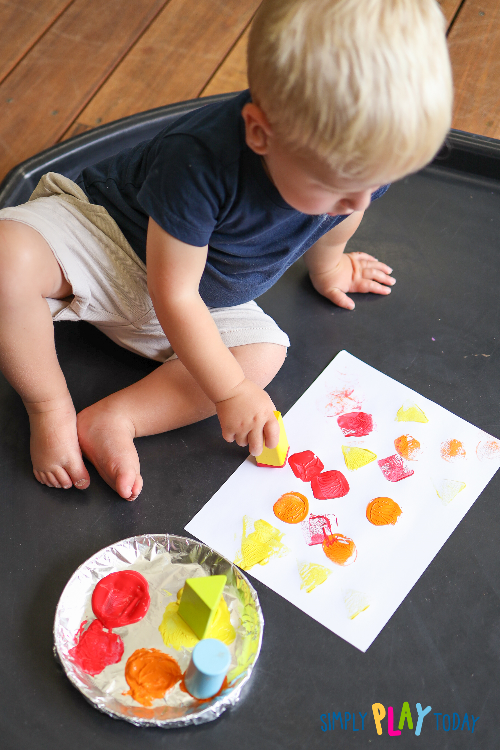 Young child dips the end of the block into a plate of paint, then stamps the blocks on the paper to leave prints